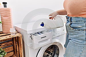 Young redhead woman pouring detegent on washing machine at laundry room