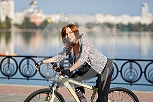 Young redhead woman riding a bike on embankment. Active people outdoors. Sport lifestyle.