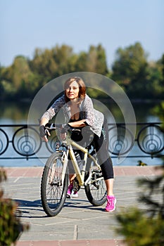 Young redhead woman riding a bike on embankment. Active people outdoors. Sport lifestyle.