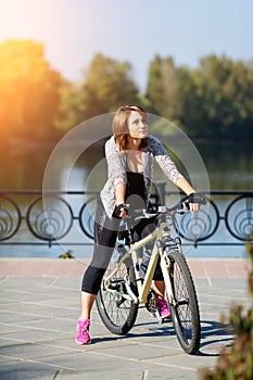 Young redhead woman riding a bike on embankment. Active people outdoors. Sport lifestyle.