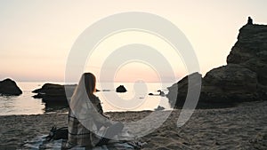 Young redhead woman sitting on the beach at sunrise, thinking and relaxing
