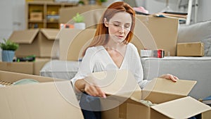 Young redhead woman sitting on floor unpacking at new home