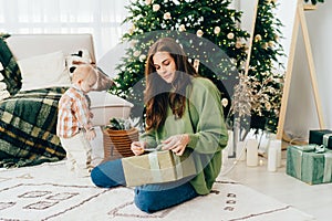 Young redhead woman sitting on the living room floor next to a Christmas tree unpacks a present.