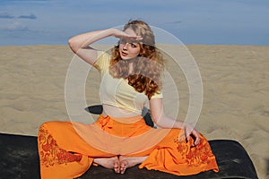 Young redhead woman sitting in purna titli yoga pose on the beach