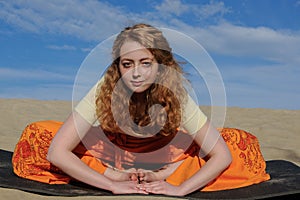 Young redhead woman sitting in purna titli yoga pose on the beach