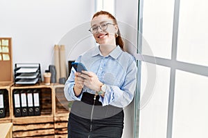 Young redhead woman smiling confident using smartphone at office