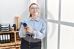 Young redhead woman smiling confident using smartphone at office
