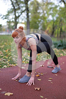 Young redhead woman in sportswear practicing sprint start and focusing on running track at autumn