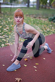 Young redhead woman in sportswear before start on running track at autumn