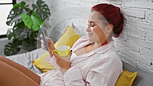 Young redhead woman using smartphone drinking coffee at bedroom