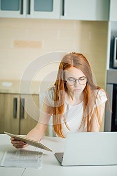 Redhead using the tablet pc and laptop in kitchen