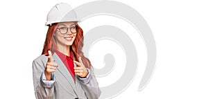 Young redhead woman wearing architect hardhat pointing fingers to camera with happy and funny face