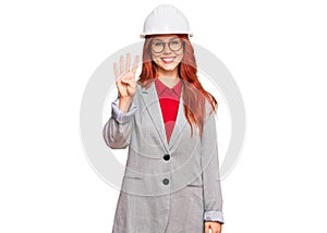 Young redhead woman wearing architect hardhat showing and pointing up with fingers number four while smiling confident and happy