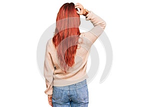 Young redhead woman wearing casual winter sweater backwards thinking about doubt with hand on head