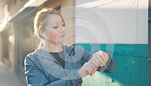 Young redhead woman wearing sportswear listening to music looking stopwatch at street