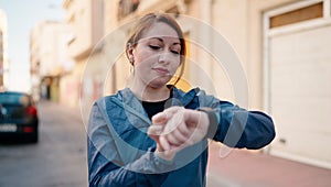 Young redhead woman wearing sportswear looking stopwatch at street