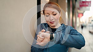 Young redhead woman wearing sportswear looking stopwatch at street
