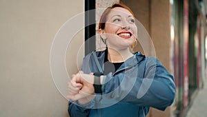 Young redhead woman wearing sportswear looking stopwatch at street