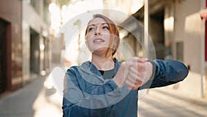 Young redhead woman wearing sportswear looking stopwatch at street