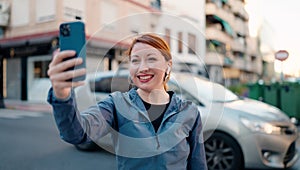 Young redhead woman wearing sportswear make selfie by smartphone looking stopwatch at street