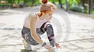 Young redhead woman wearing sportswear tying shoes at park