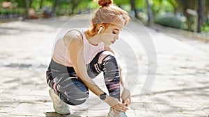 Young redhead woman wearing sportswear tying shoes at park