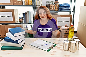 Young redhead woman wearing volunteer t shirt at donations stand smiling cheerful with open arms as friendly welcome, positive and