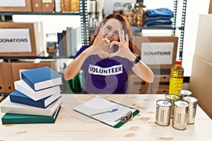 Young redhead woman wearing volunteer t shirt at donations stand smiling in love doing heart symbol shape with hands