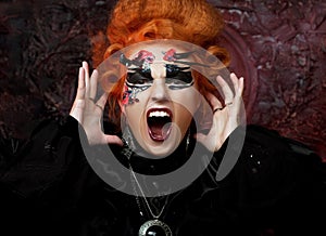 Young redhead woman in witch costume screams and rages. Halloween and party concept