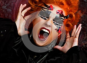 Young redhead woman in witch costume screams and rages. Halloween and party concept.