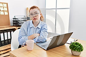 Young redhead woman working at the office using computer laptop looking sleepy and tired, exhausted for fatigue and hangover, lazy