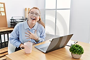 Young redhead woman working at the office using computer laptop smiling and laughing hard out loud because funny crazy joke with