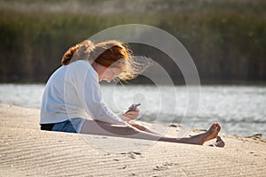 Young redheaded girl using a phone beside a river at the beach