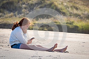 Young redheaded girl using a phone beside a river at the beach
