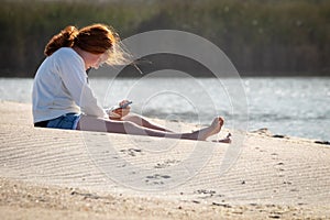 Young redheaded girl using a phone beside a river at the beach