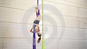 Young redheaded woman doing aerial gymnastic acrobatics with acrobatic fabrics inside a gym.