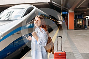 Young redhhead woman waiting train with backpack and using smart phone. Railroad transport concept, Traveler.Woman with