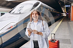 Young redhhead woman waiting train with backpack and using smart phone. Railroad transport concept, Traveler.Woman with