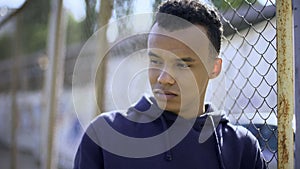 Young refugee from dysfunctional family leaning on fence, orphan teenager photo