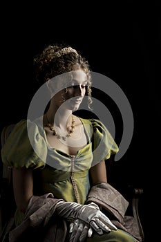 A young Regency woman wearing a green shot silk dress and sitting in front of a dark backdrop