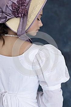 A young Regency woman wearing a white muslin dress, straw bonnet, and a pearl necklace photo