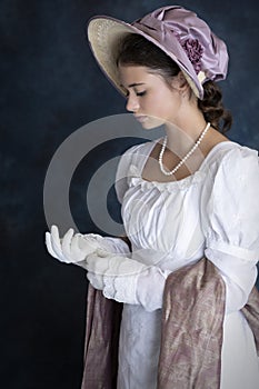 A young Regency woman wearing a white muslin dress, straw bonnet, and a pearl necklace