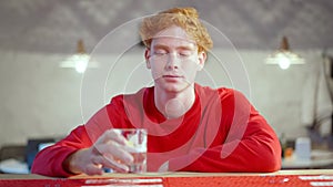 Young relaxed Caucasian man clinking and looking at camera. Portrait of redhead Caucasian millennial resting in bar or