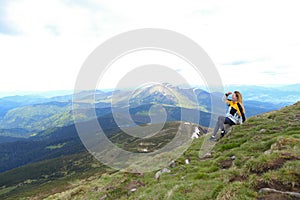 Young relaxed female tourist wearing yellow jacket sitting in Appenine mountains.