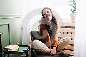 Young relaxed smiling pretty woman relaxing sitting on chair at home. Happy positive beautiful lady feeling joy enjoying wellbeing