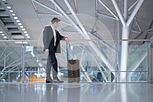 Young relaxed traveling businessman standing next to his luggage