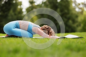 Young relaxed woman lying on yoga mat with face down in relaxing childs pose outdoors in park