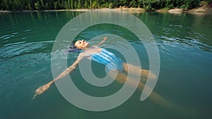 Young relaxed woman swimming on back in beautiful mountain lake with clear blue water
