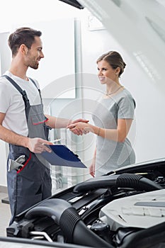 Young repair worker shaking hands with customer in car workshop