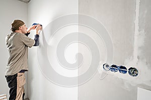 Young repairman aligns with plastic spatula. Worker glueing wallpapers on concrete wall. Repair the apartment. Home